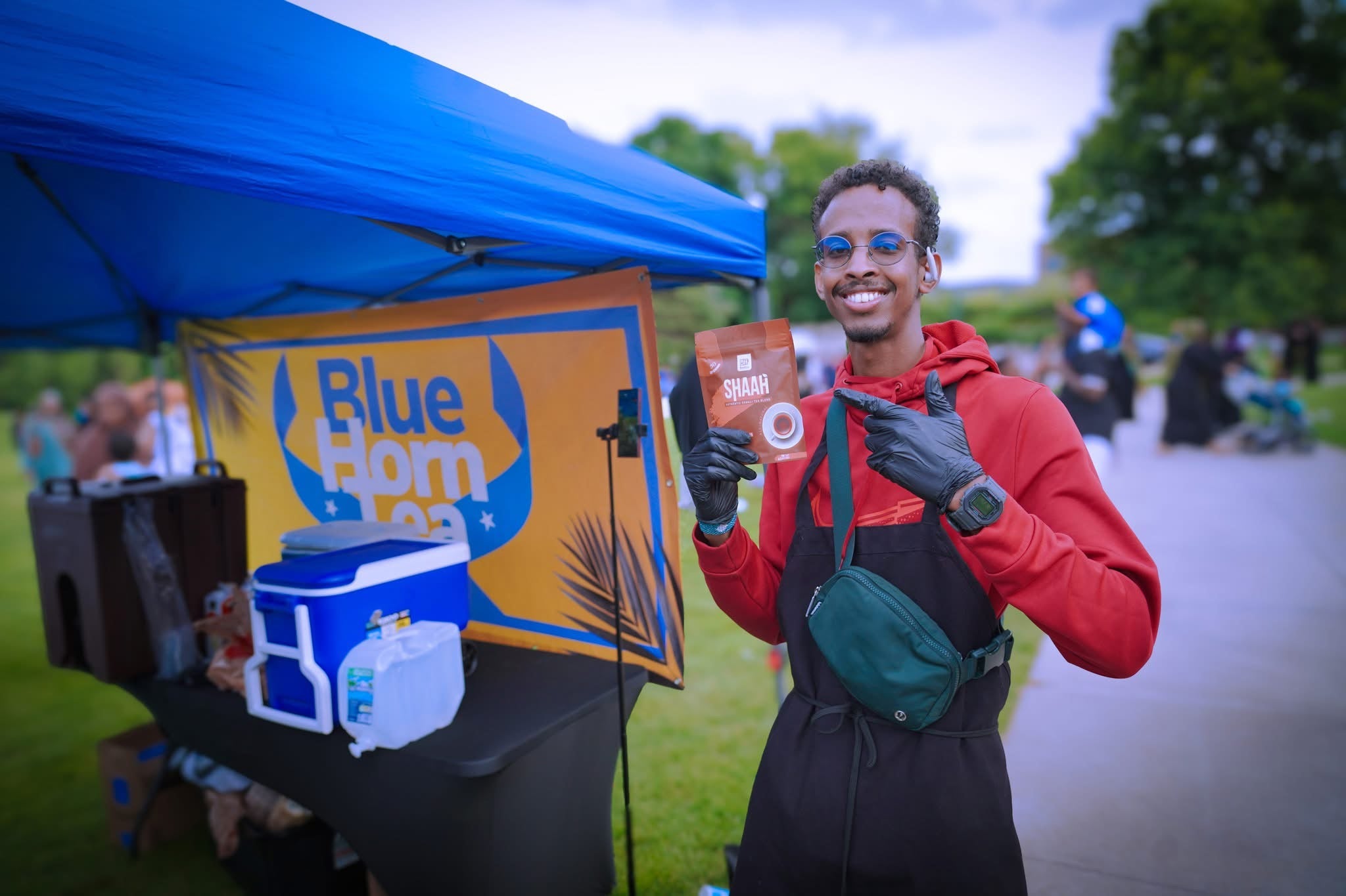 Yubi smiling and holding a pouch of Shaah at a community market